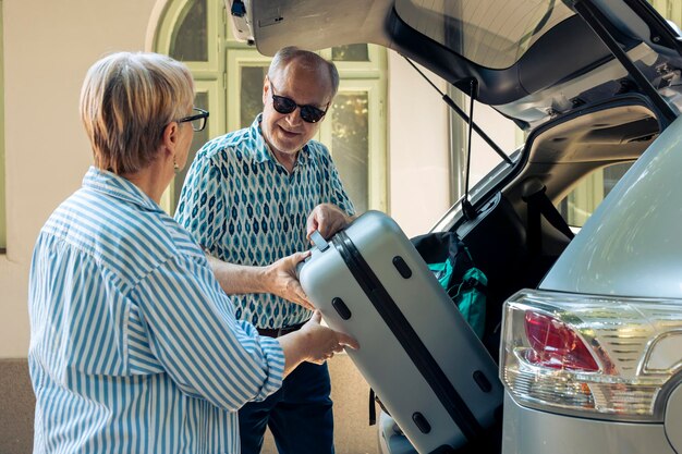 Persone anziane che caricano il carrello nel bagagliaio dell'auto, viaggiando in vacanza in pensione durante l'estate. Persone anziane che partono per un'avventura su strada, mettendo valigie e borse da viaggio.