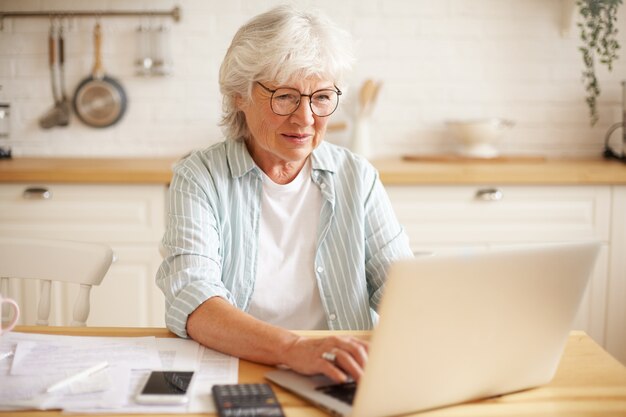 Persone anziane, gadget elettronici e concetto di stile di vita. Ritratto di donna eccitata in pensione acquisti online utilizzando laptop. Donna anziana che ha uno sguardo felice perché ha finalmente saldato tutti i suoi debiti