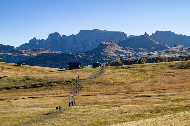 Persone che camminano su un sentiero in mezzo a campi erbosi con edifici in lontananza