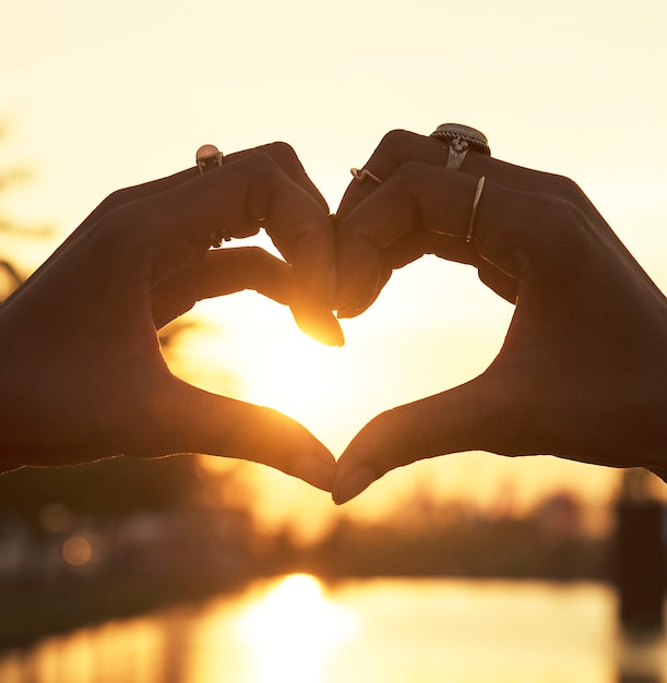 Persone che fanno un cuore con le mani al tramonto