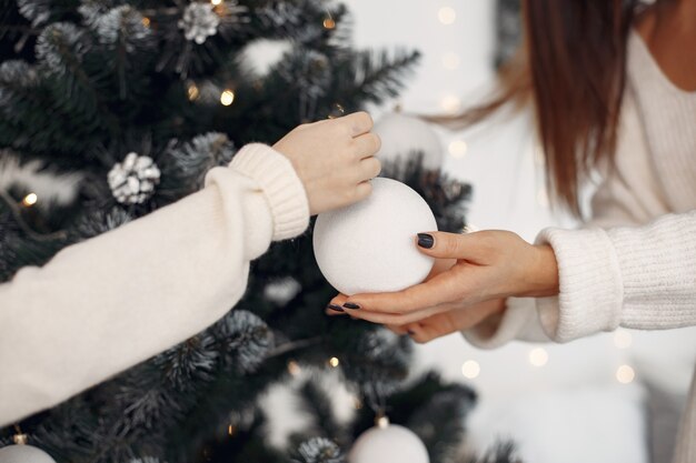 Persone che si preparano per il Natale. Madre che gioca con sua figlia. Albero di Natale decorato in famiglia. Bambina in un vestito bianco.