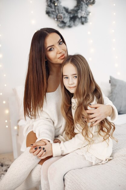 Persone che si preparano per il Natale. Madre che gioca con sua figlia. Famiglia seduta su un letto. Bambina in un vestito bianco.