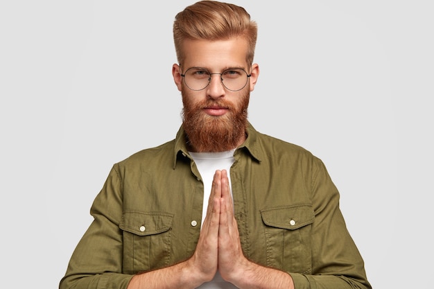 Persone e concetto di religione. I giovani hipster con la barba lunga seri tengono le mani nel gesto di preghiera