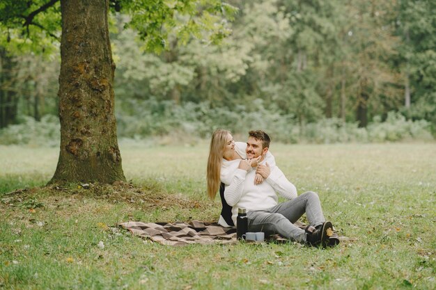 Persone in un parco. Donna in un cappotto marrone. Uomo con un maglione bianco. Coppia in un picnic.