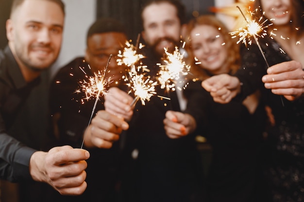 Persone in una decorazione Christman. Uomo in abito nero. Celebrazioni di gruppo Capodanno. Persone con luci bengala.