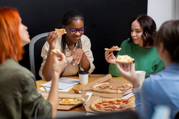 Persone sorridenti che mangiano pizza al lavoro
