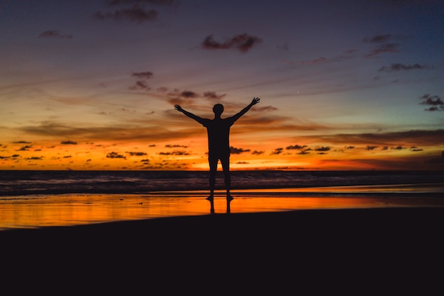 persone sulla riva dell&#39;oceano al tramonto. l&#39;uomo salta sullo sfondo del sole al tramonto