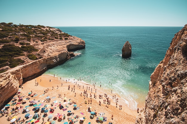 Persone sulla spiaggia di sabbia vicino alle scogliere e al mare calmo