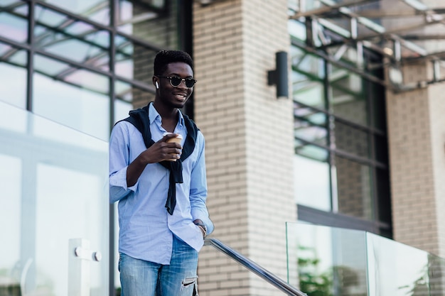 Persone, tecnologia e stile di vita - giovane felice con cuffie e smartphone che ascolta musica in città con una tazza di caffè.