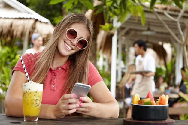 Persone, tecnologia moderna e concetto di comunicazione. Bella ragazza in tonalità alla moda che invia messaggi di testo agli amici, controllando il feed di notizie tramite i social media mentre navighi in Internet al caffè