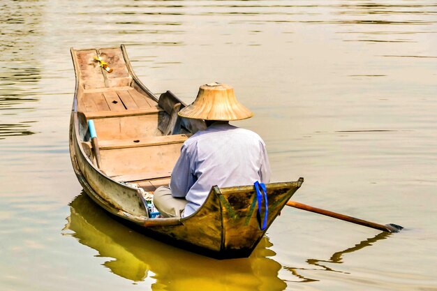 Pescatore in un cappello a cono asiatico che naviga nel lago con una piccola barca di legno