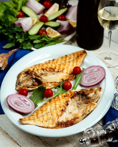 Pesce alla griglia tagliato a metà servito con cipolla e pomodorini