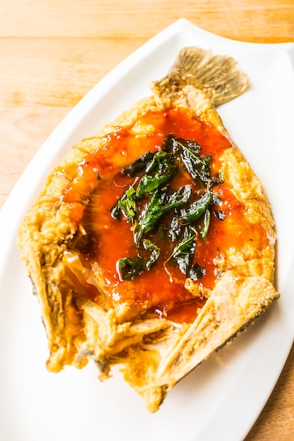 Pesce branzino fritto in piatto bianco con salsa piccante e dolce
