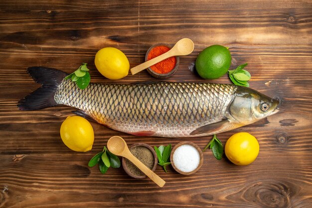 Pesce fresco vista dall'alto con limone e condimenti sulla scrivania in legno