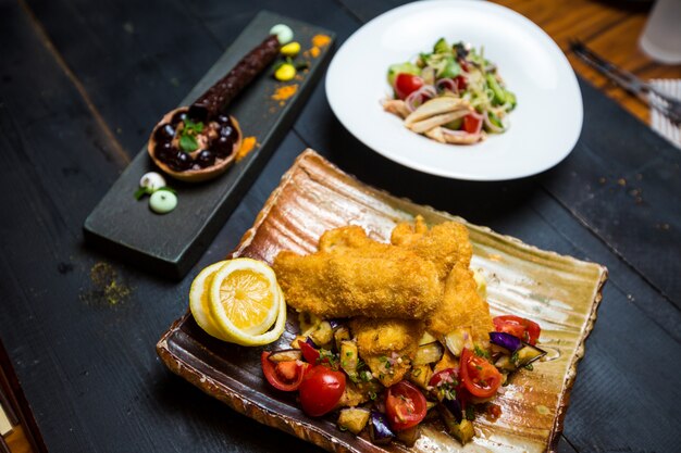 Pesce fritto croccante servito con melanzane fritte e insalata di pomodori freschi