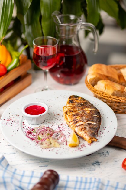 Pesce grigliato arrosto servito con erbe, limone, insalata di cipolle e salsa di pomodoro rosso.