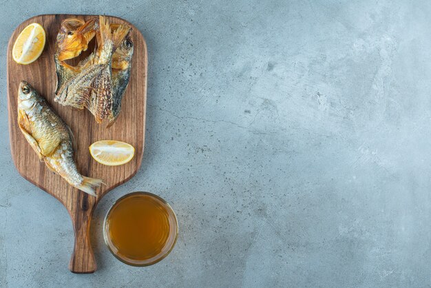 Pesce, limone a fette un bicchiere di birra a bordo su marmo.