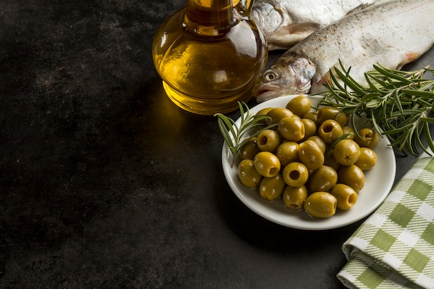 Pesce, olio d&#39;oliva e olive su superficie scura