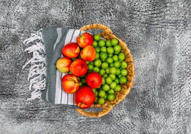 Pesche e greengages in un canestro di vimini e panno di picnic su gray di lerciume. vista dall'alto.