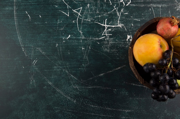 Pesche e uva in una ciotola di legno sul bordo nero