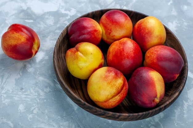 Pesche fresche di mezza vista con frutti morbidi e gustosi all'interno del piatto marrone sulla scrivania bianco-chiaro, frutta fresca, foto, vitamina