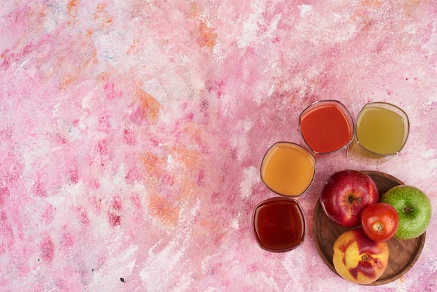 Pesche, pomodori e mele con tazze di succo su tavola di legno, vista dall'alto.