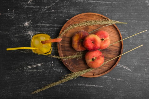 Pesche rosse con un bicchiere di succo in un piatto di legno, vista dall'alto