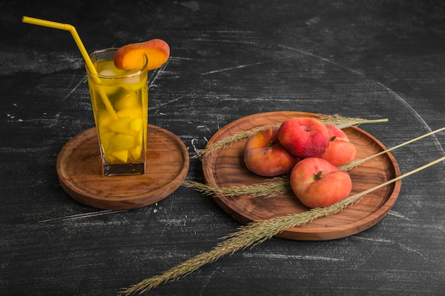 Pesche rosse con un bicchiere di succo in un piatto di legno