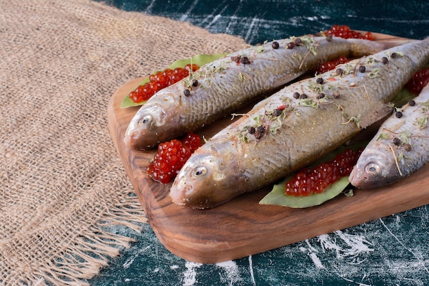 Pesci interi crudi con caviale rosso su tavola di legno.