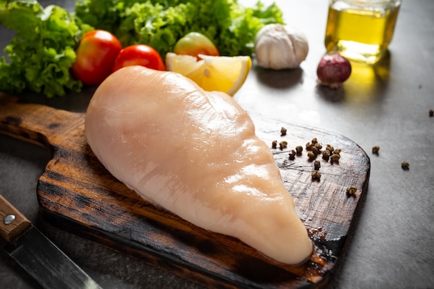 Petti di pollo crudi sul tagliere di legno.