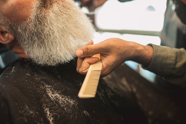 Pettinare i capelli grigi del cliente anziano nel negozio di barbiere