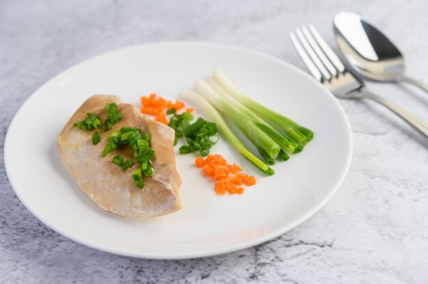 Petto di pollo al vapore su un piatto bianco con cipollotti e carote tritate