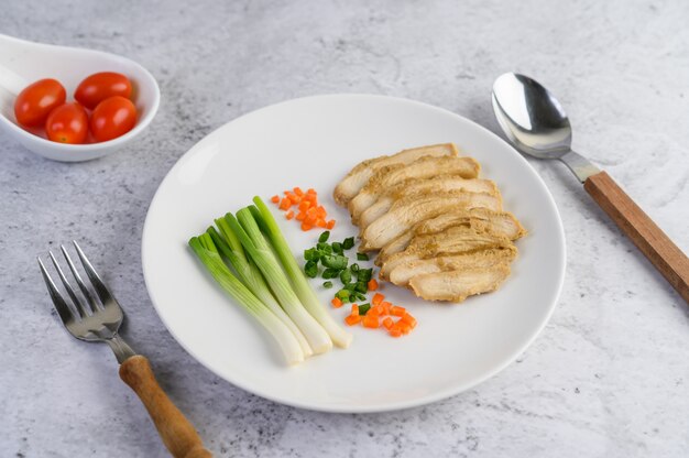 Petto di pollo al vapore su un piatto bianco con cipollotti e carote tritate