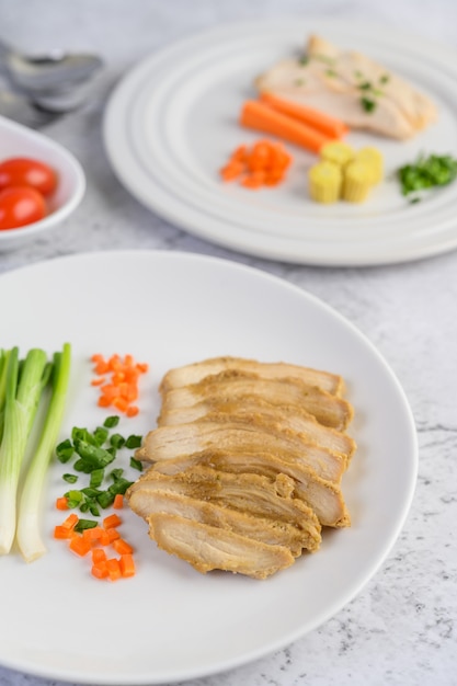 Petto di pollo al vapore su un piatto bianco con cipollotti e carote tritate