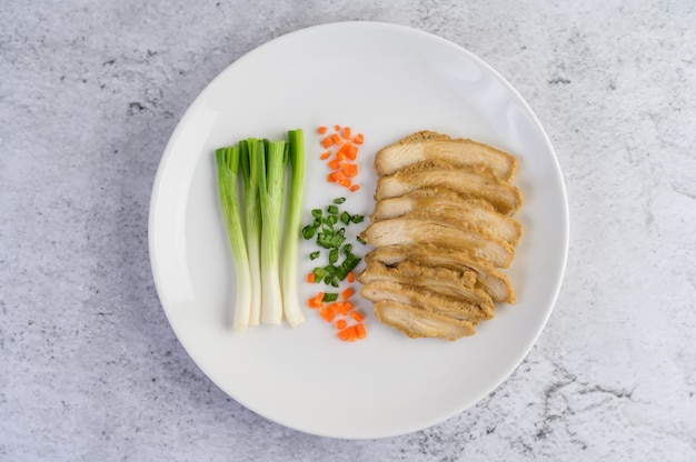Petto di pollo al vapore su un piatto bianco con cipollotti e carote tritate