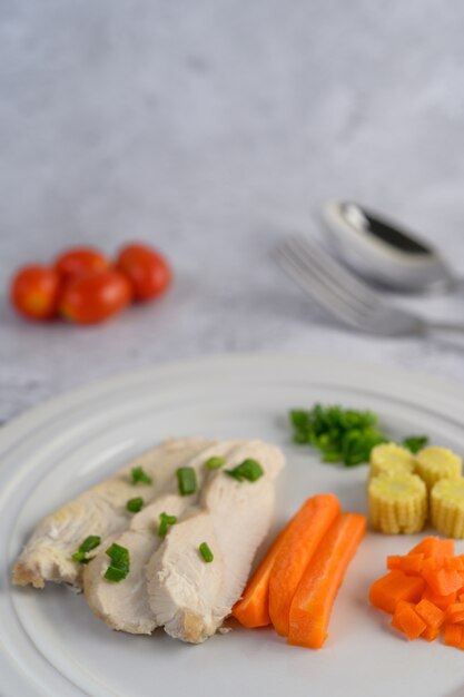 Petto di pollo al vapore su un piatto bianco con cipollotti, mais e carote tritate.