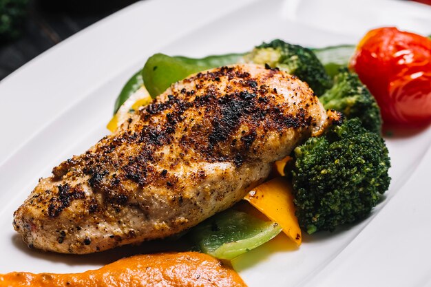 Petto di pollo arrostito di vista laterale con peperone dei broccoli e pomodoro con peperone verde caldo e salsa