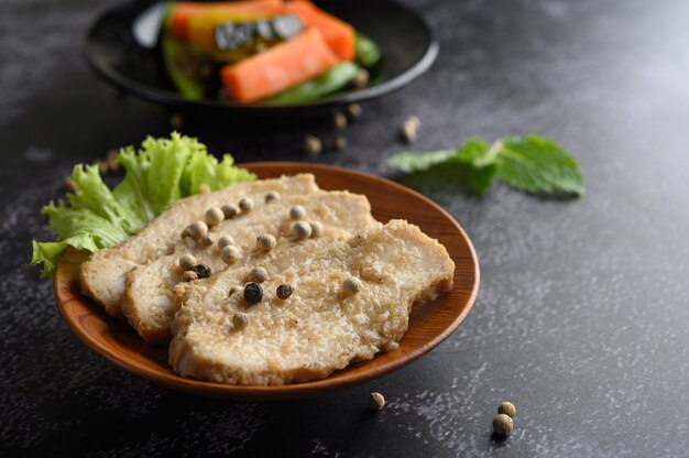 Petto di pollo grigliato, cosparso di pepe, posto su un piatto di legno