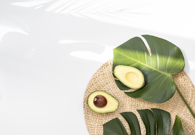 Pezzi di avocado su un pavimento di fibre naturali e ha uno sfondo di natura Foglia di monstera tropicale