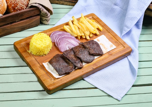 Pezzi di bistecca di carne con patatine fritte, cipolla e riso.