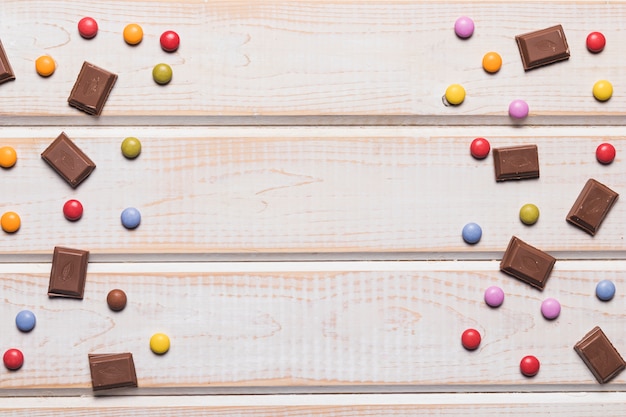 Pezzi di cioccolato e gemme colorate su sfondo con texture in legno con spazio di copia per la scrittura del testo