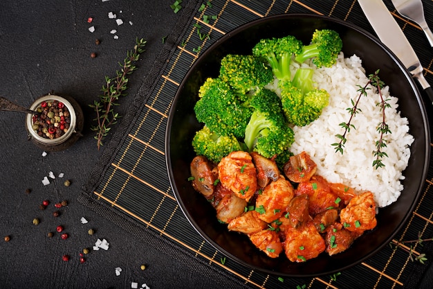 Pezzi di filetto di pollo con funghi in umido in salsa di pomodoro con broccoli e riso bolliti. Nutrizione appropriata. Uno stile di vita sano. Menu dietetico. Vista dall'alto