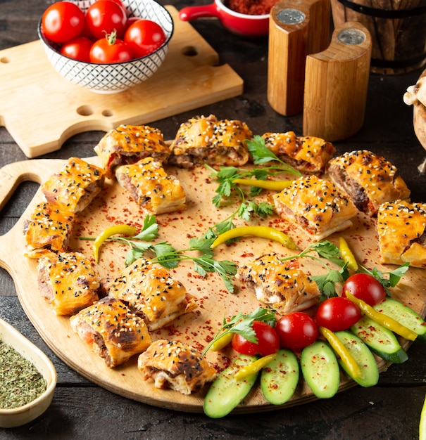 pezzi di kebab beyti serviti su tavola di legno con cetrioli e pomodori