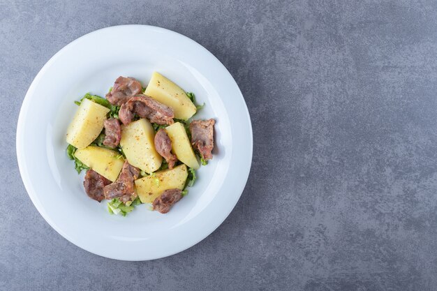 Pezzi di kebab e patate bollite sul piatto bianco.