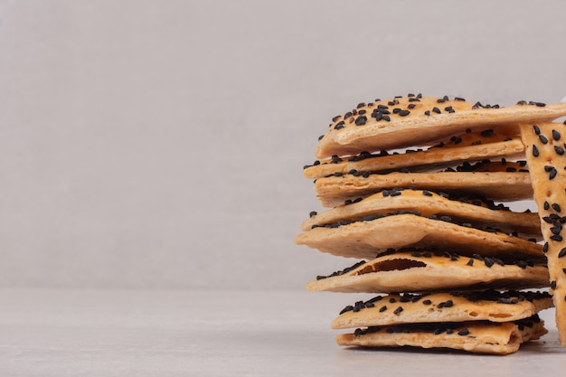 Pezzi di pane croccante con semi di sesamo nero su bianco.