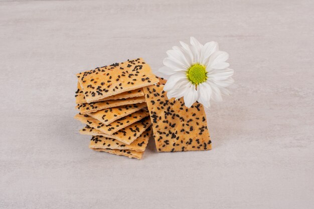 Pezzi di pane croccante con semi di sesamo nero su fondo bianco con fiore.