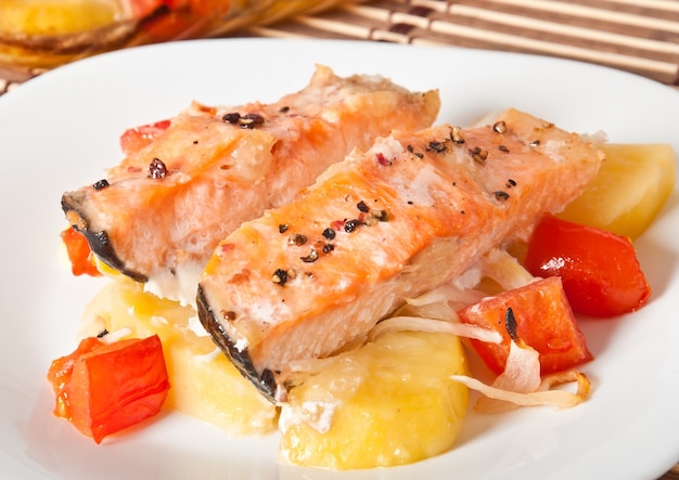 Pezzi di salmone con patate, pomodori e cipolle al forno