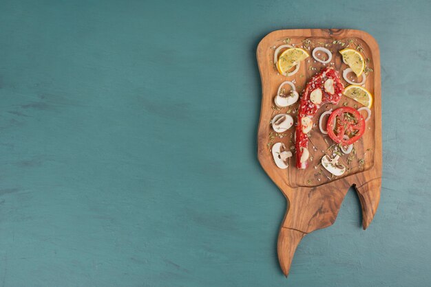 Pezzo di carne cruda con verdure sul tavolo blu.