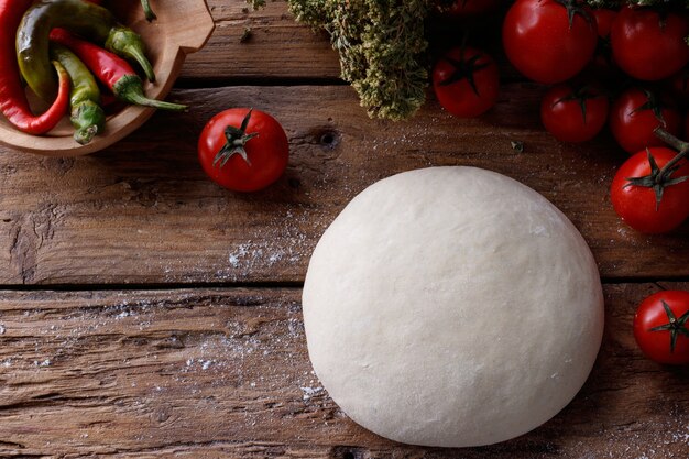 Pezzo di pasta su un tavolo di legno circondato da pomodori e pepe