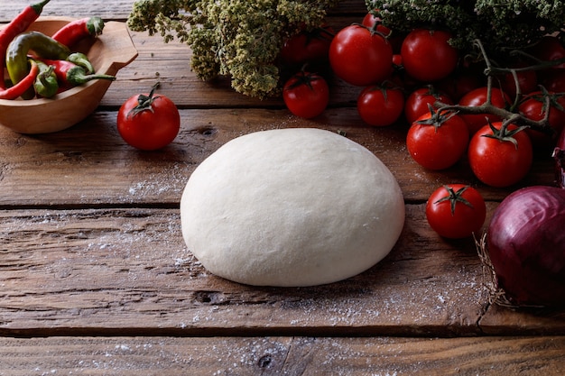 Pezzo di pasta su un tavolo di legno circondato da pomodori, pepe e cipolla